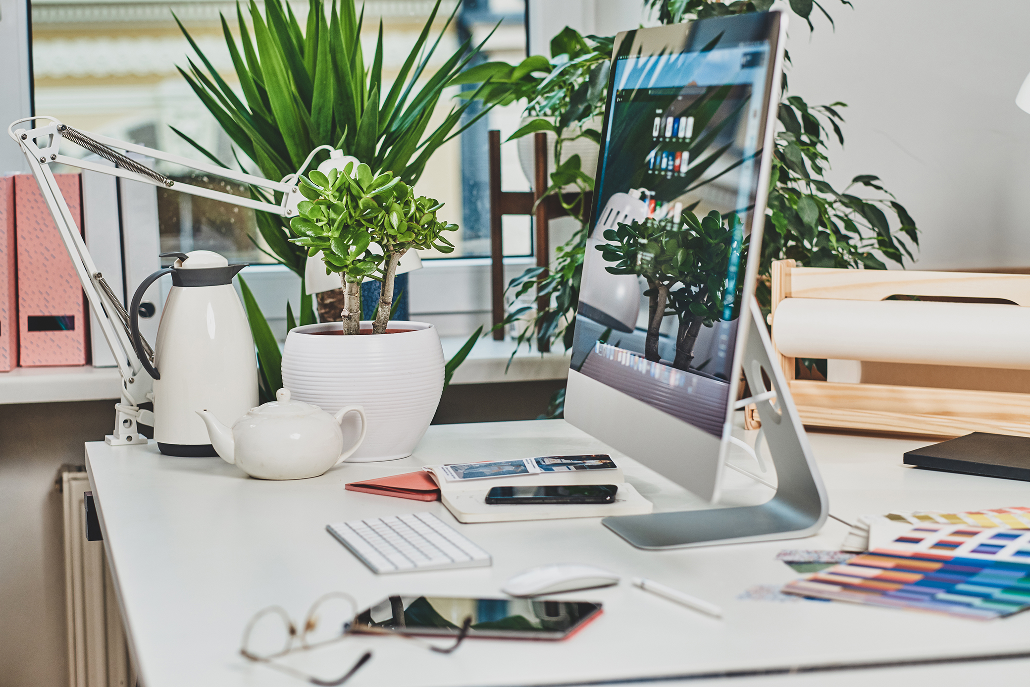 Modern bright office with computer on the table with plants, kettle, mobile phone and keyboard.